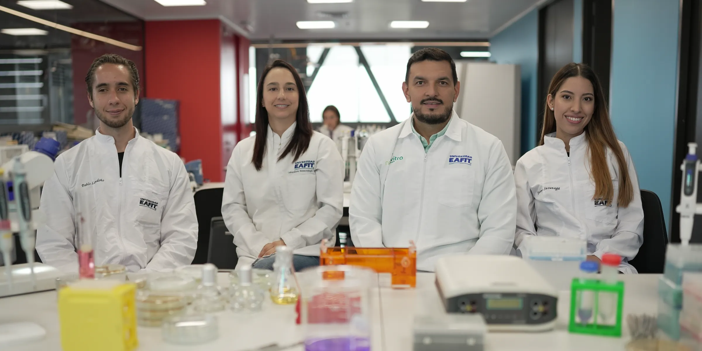 Pablo Londoño, Martha Catalina Restrepo, Diego F. Villanueva y Danna Susunaga, en bata, sentados tras una mesa de laboratorio.